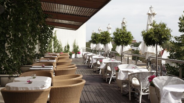 An outdoor dining area with wicker furniture and white umbrellas. - Rija VEF Hotel (Riga)