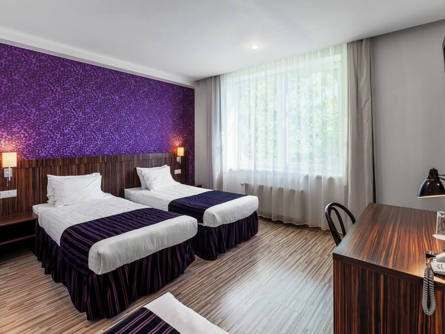 A hotel room with two beds, a desk, a chair, and a large window with curtains.