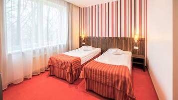 A hotel room with two beds, a large window with sheer curtains, a striped wall panel, and a red carpet.