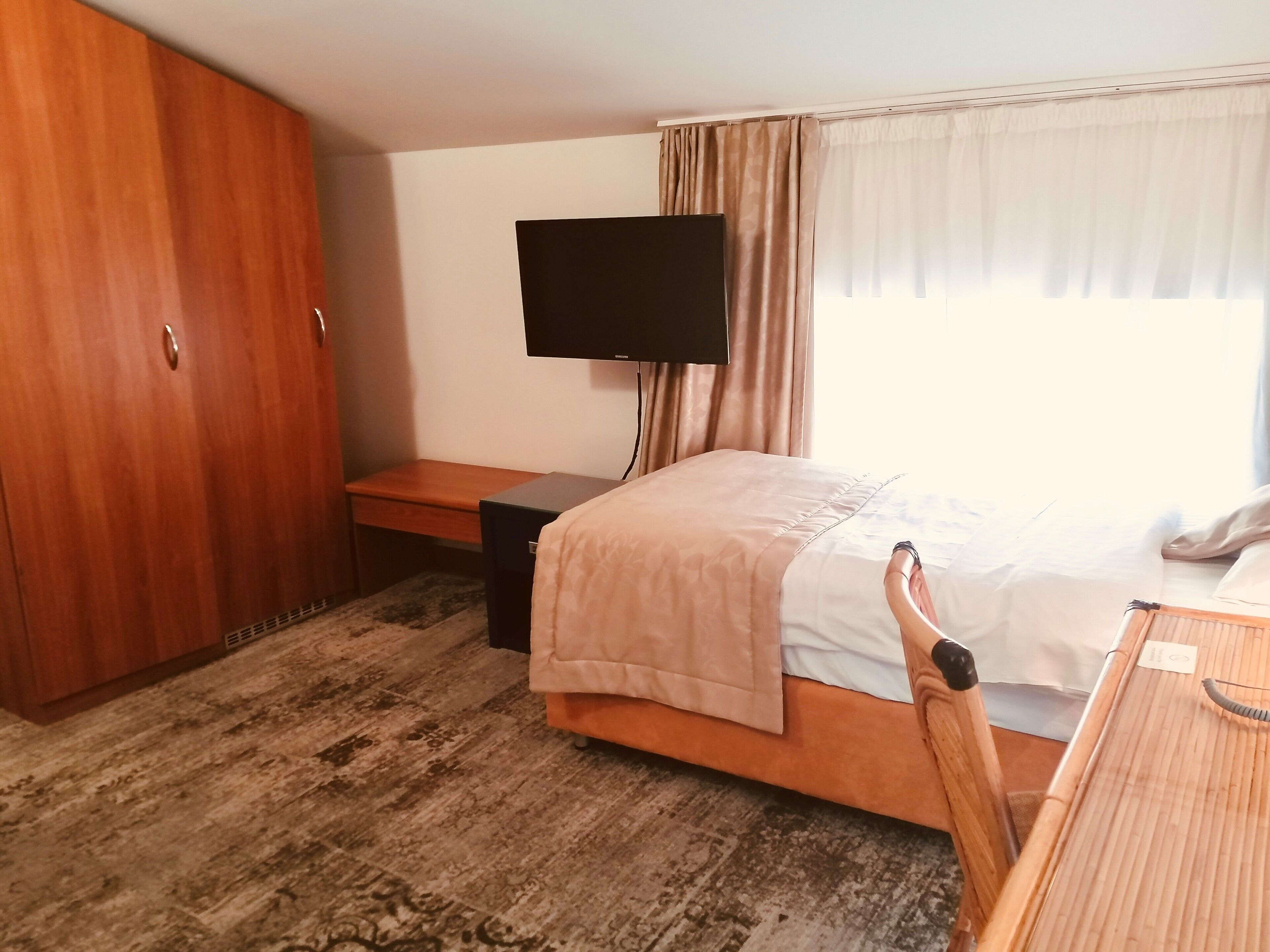Una habitación de hotel con una cama, un escritorio, un televisor y un armario.