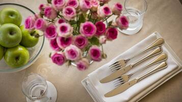 A table setting with a bowl of green apples, a vase of pink roses, and a glass of water.