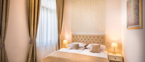 Habitación de hotel con una cama grande, dos mesitas de noche con lámparas, un cabecero decorativo y un cuadro en la pared.