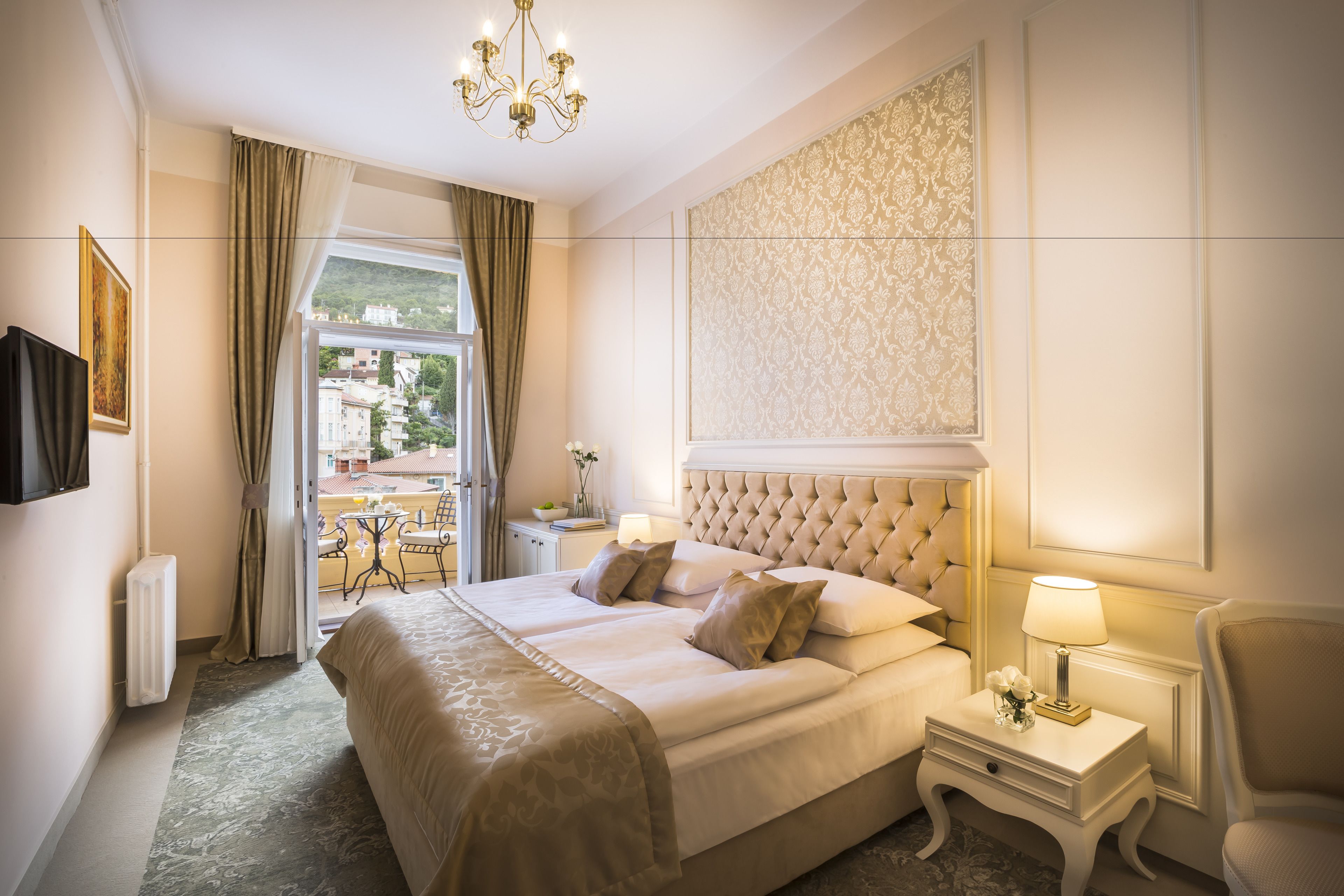 Camera d'albergo con un letto grande, un comodino con una lampada, una sedia e vista sull'esterno.