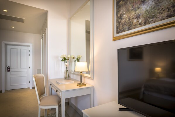Habitación de hotel con un escritorio blanco, una silla, un televisor y un espejo grande.