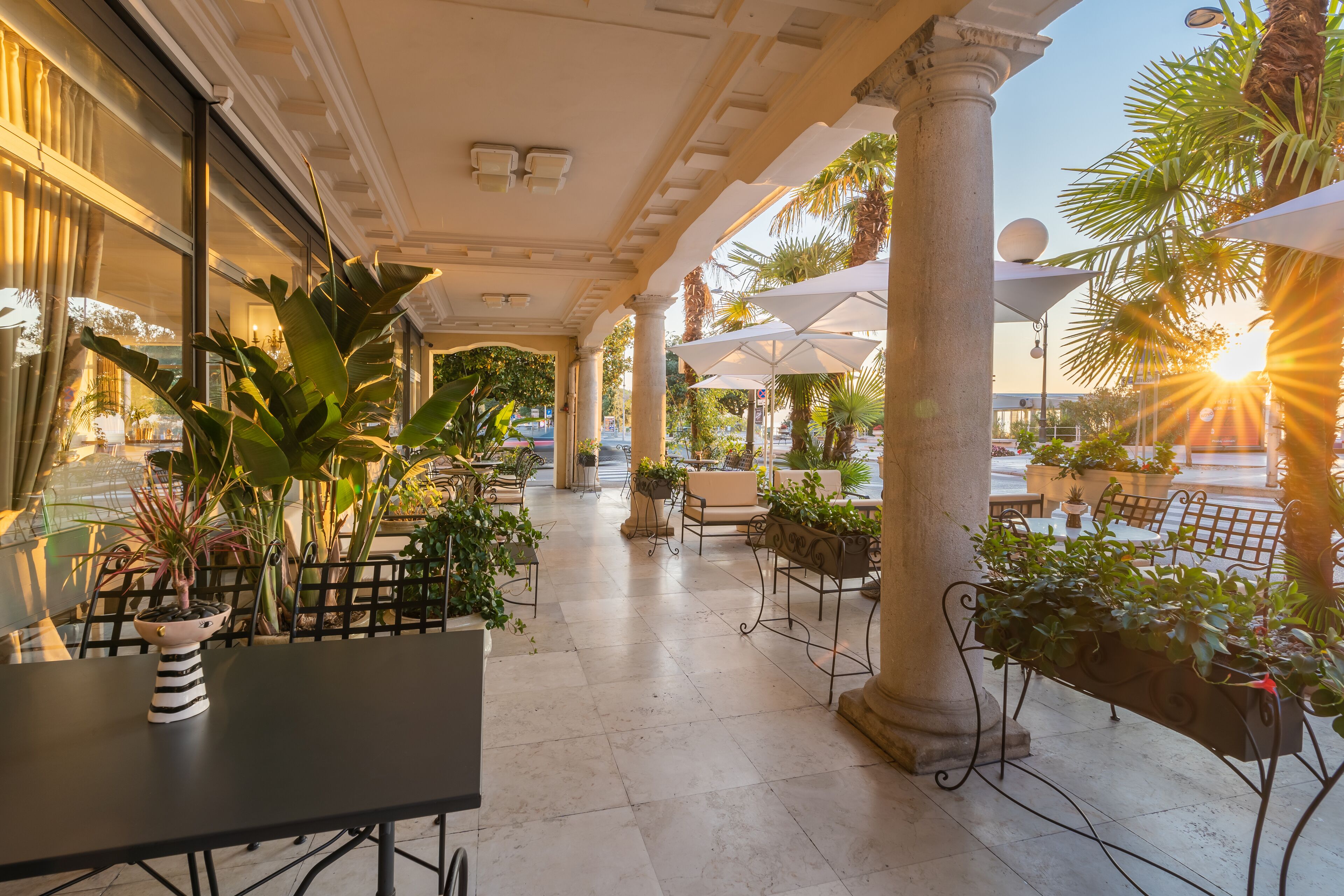 An outdoor patio area with tables and chairs, surrounded by columns and potted plants.