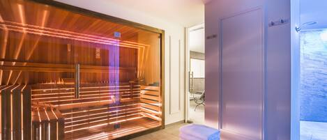 A modern sauna room with wooden benches and a glass enclosure. There are towels stacked on a table.