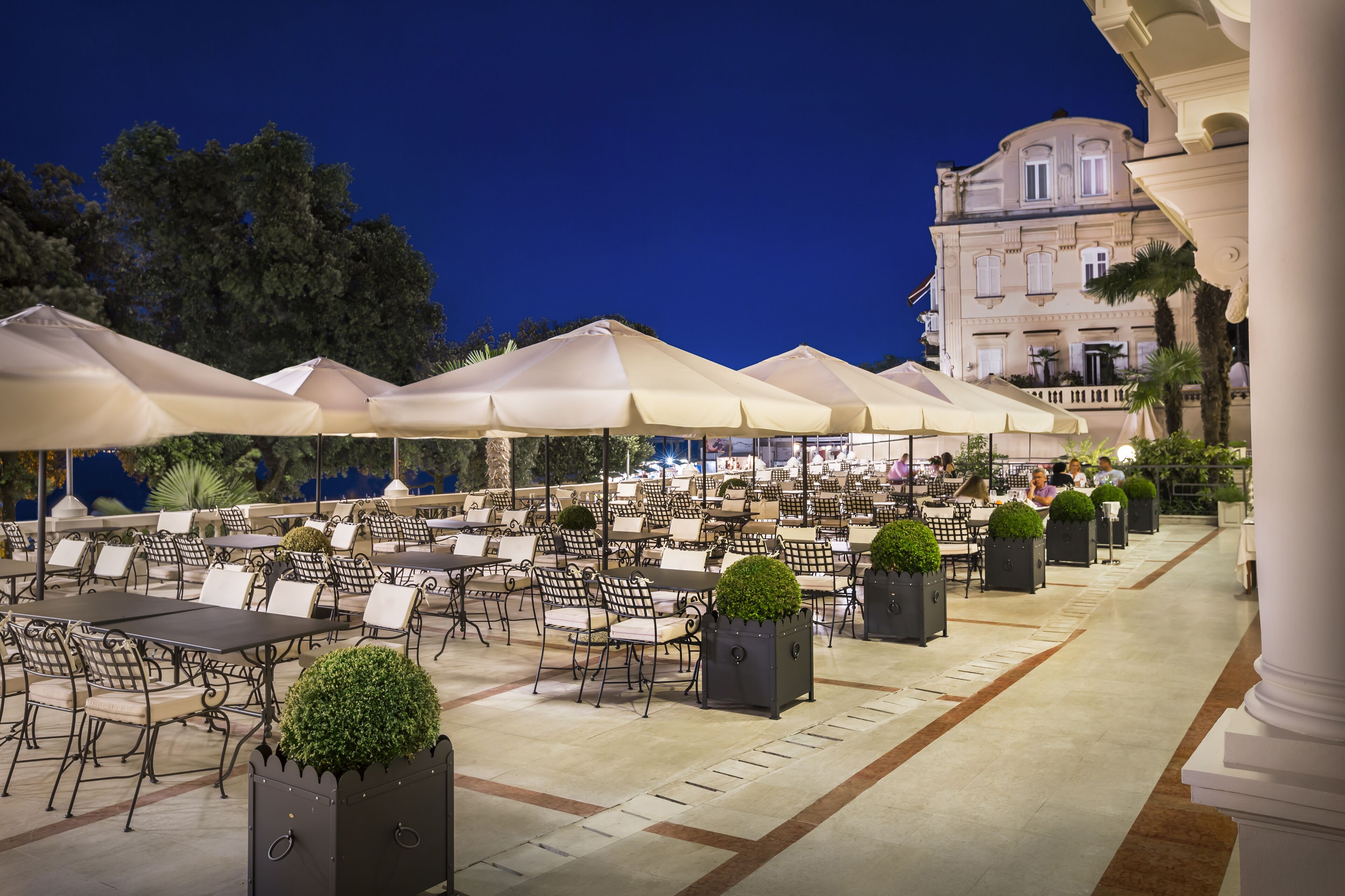 An outdoor cafe with tables and chairs, umbrellas, and planters.