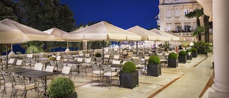 An outdoor cafe with tables and chairs, umbrellas, and planters.