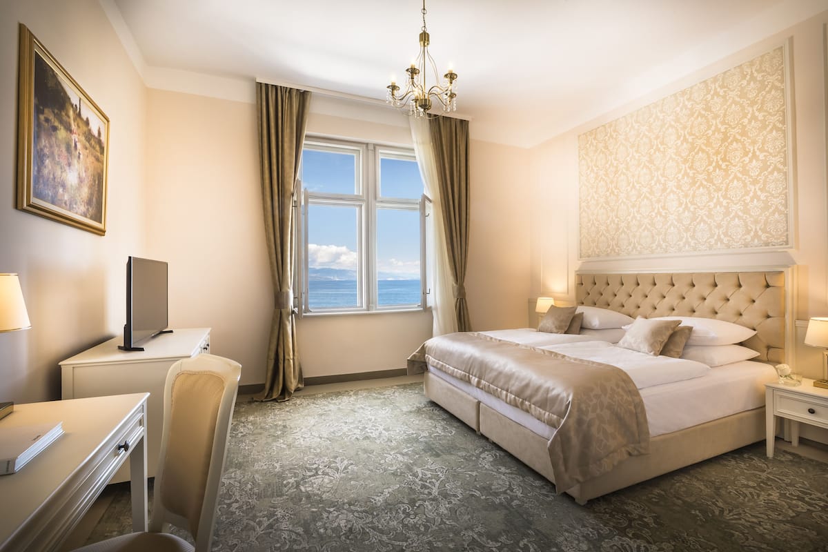 Ein Hotelzimmer mit einem großen Bett, einem Schreibtisch, einem Sessel, einem Fernseher und Blick aufs Meer.