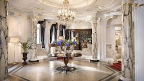 Een statige lobby met marmeren zuilen, een kroonluchter en een decoratief element in het midden van de vloer.