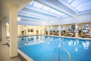 An indoor swimming pool with a skylight, lounge chairs, and potted plants.