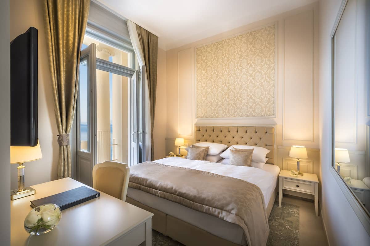 Ein Hotelzimmer mit einem großen Bett, zwei Nachttischen mit Lampen, einem Flachbildfernseher, einem Schreibtisch mit einem Laptop und einer Blumenvase.
