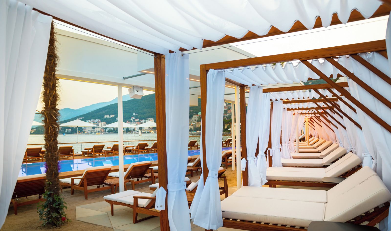A sunlit indoor pool area with wooden loungers and a canopy structure.