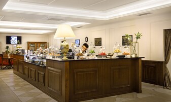 Uma área de recepção de hotel com um balcão de madeira, uma luminária grande e diversos alimentos expostos em cúpulas de vidro.