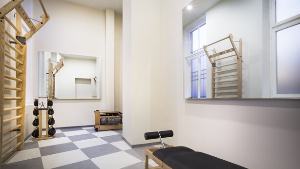 Een sportschool met een geruit vloerkleed, houten trainingsapparatuur en een bank.