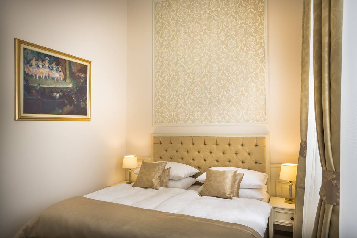Ein Hotelzimmer mit einem großen Bett, zwei Nachttischen mit Lampen, einem Bild an der Wand und einer gemusterten Tapete über dem Bett.