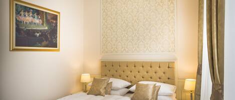 A hotel room with a large bed, two bedside tables with lamps, a painting on the wall, and a patterned wallpaper above the bed.