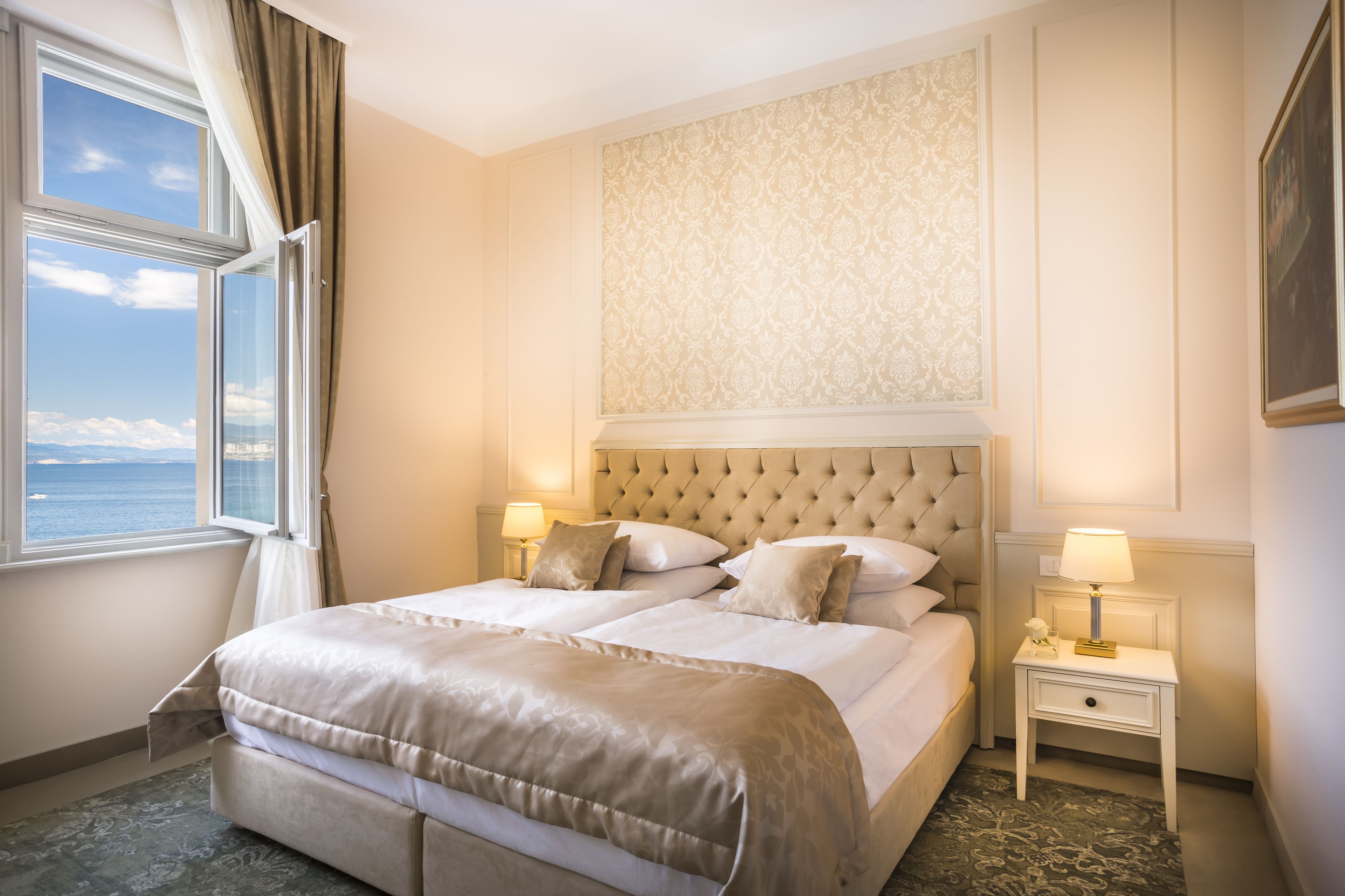 Une chambre d’hôtel avec un grand lit, deux tables de chevet, une fenêtre avec des rideaux et une vue sur la mer.