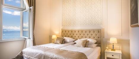 Une chambre d’hôtel avec un grand lit, deux tables de chevet, une fenêtre avec des rideaux et une vue sur la mer.