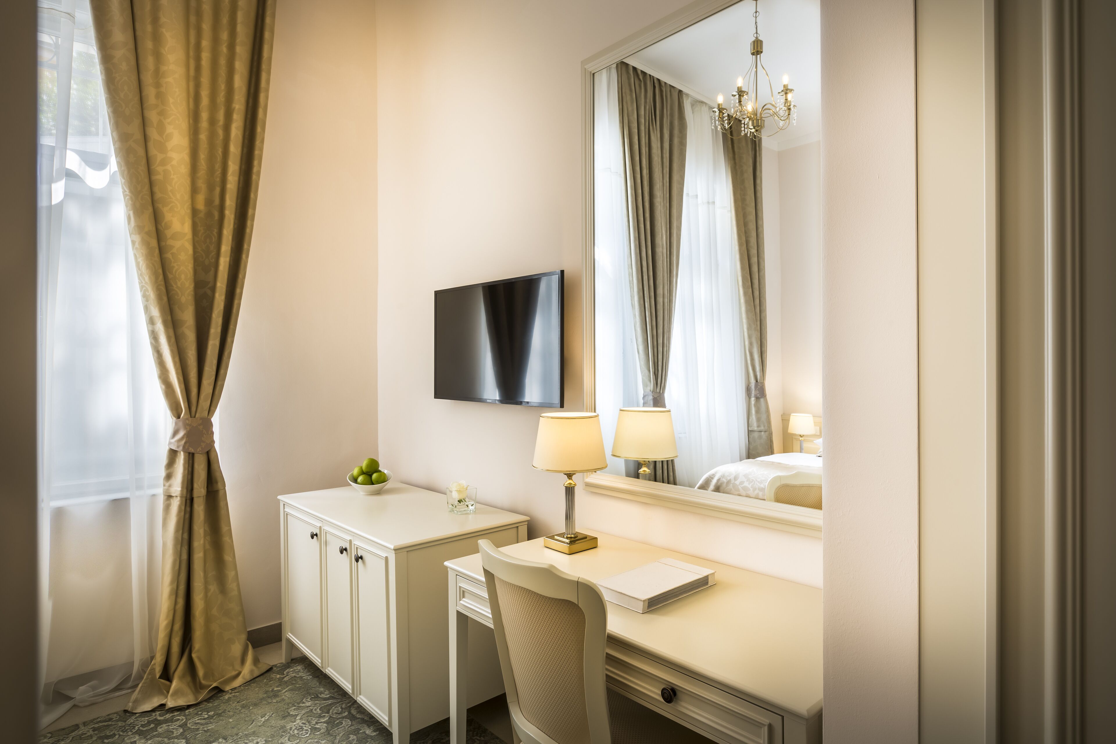 Una habitación de hotel con cama, escritorio, silla, televisor y candelabro.