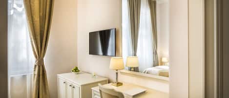 A hotel room with a bed, a desk with a chair, a television, and a chandelier.
