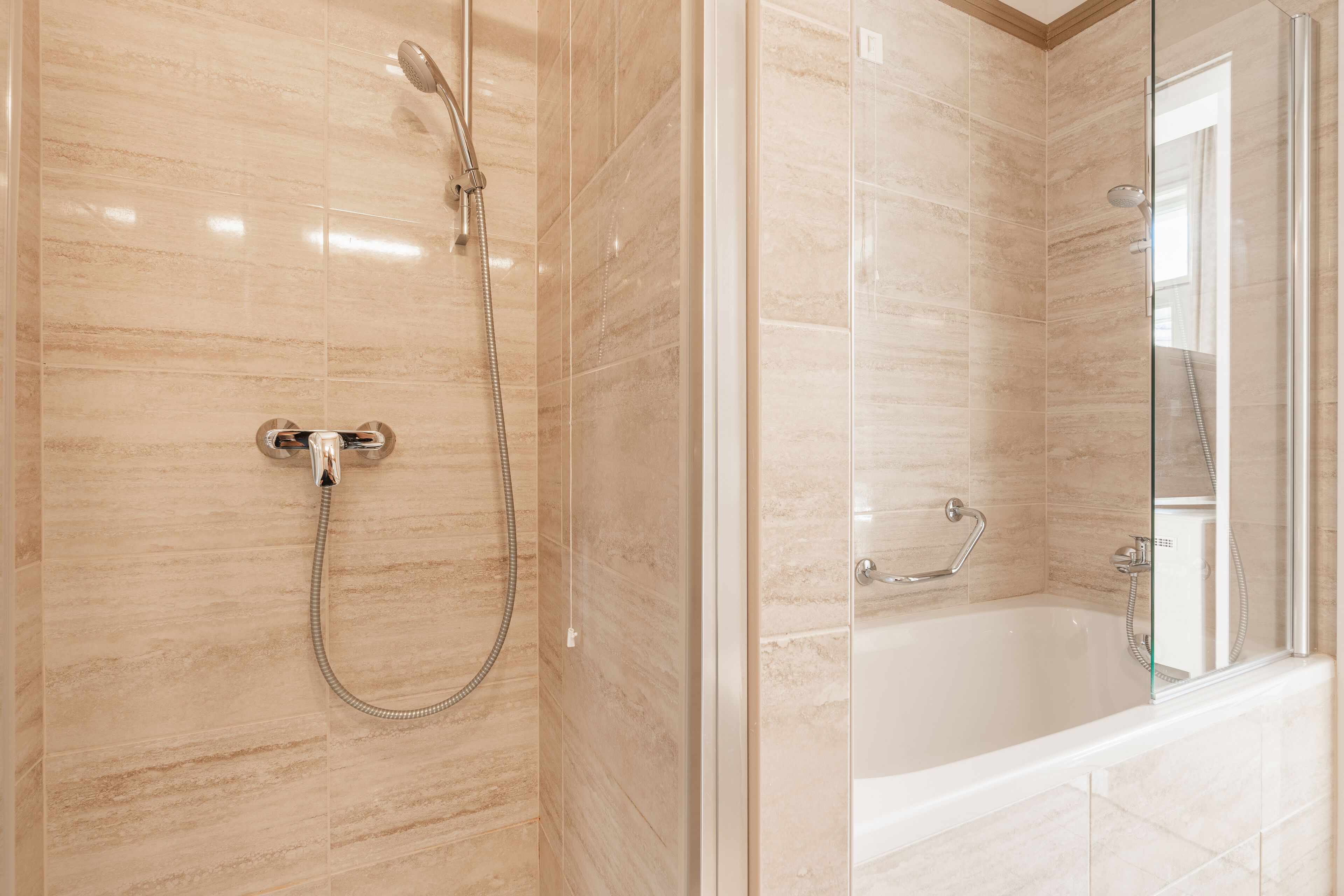 A modern bathroom with a glass-enclosed shower, a separate bathtub, and a tiled floor.