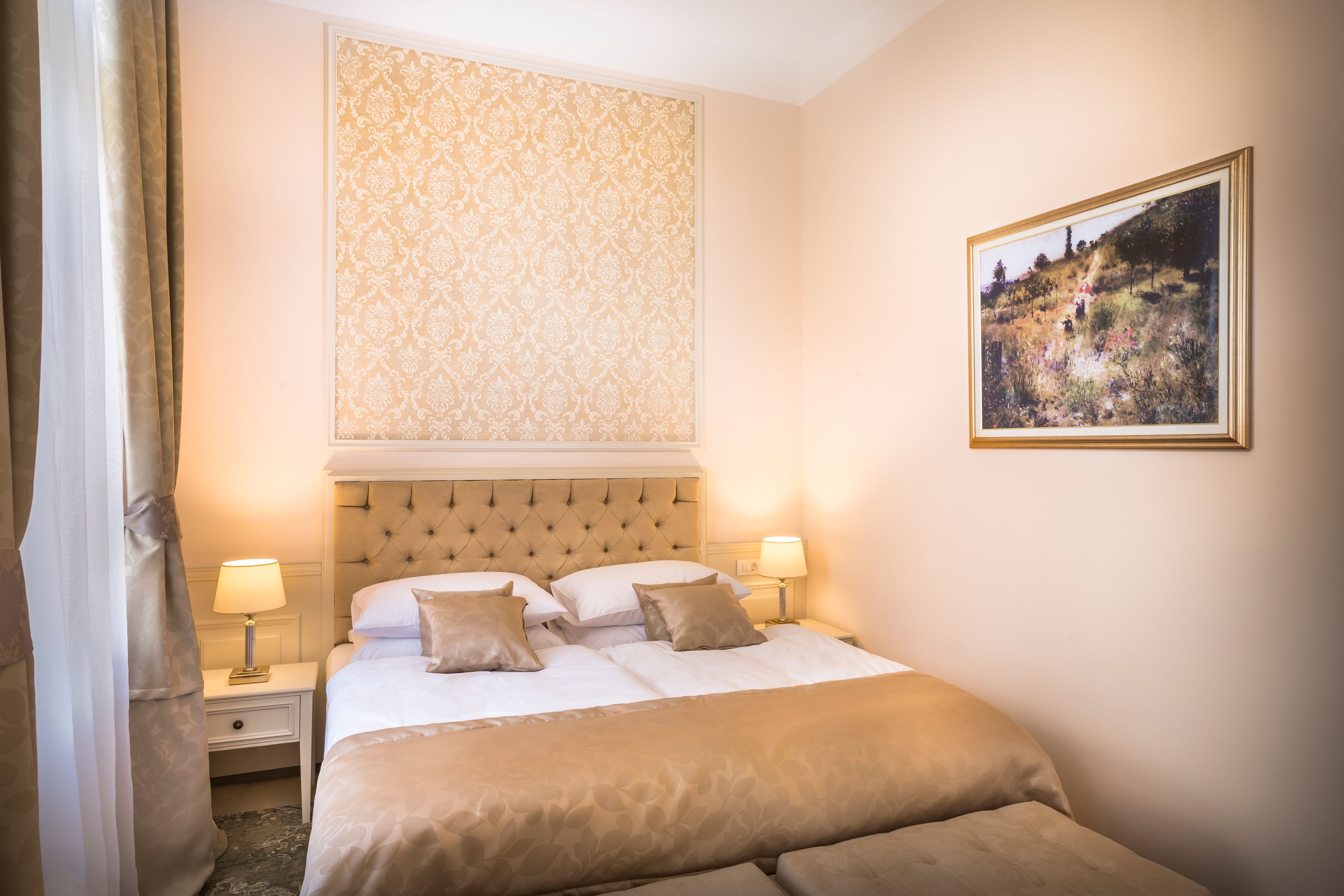 Een hotelkamer met een groot bed, twee nachtkastjes met lampen, een hoofdbord, een behang met patroon en een inlijstbaar schilderij aan de muur.