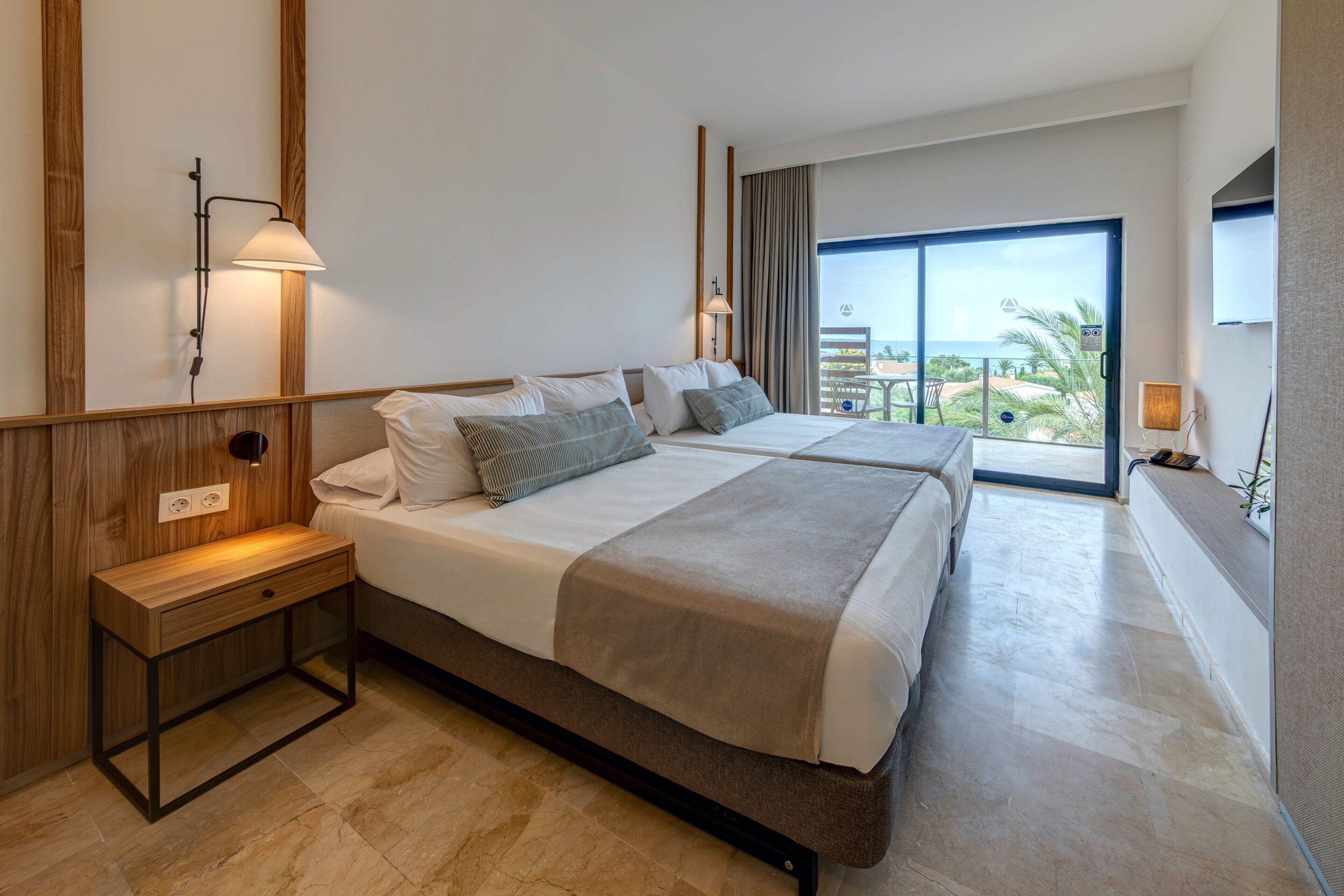 Habitación de hotel con cama, mesitas de noche, escritorio y vistas al exterior.