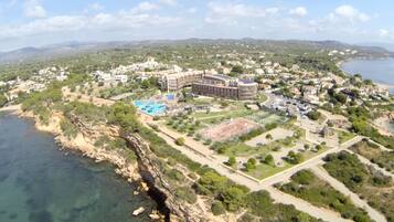 Vista aérea de un complejo turístico costero con un edificio grande, una piscina y vegetación circundante.