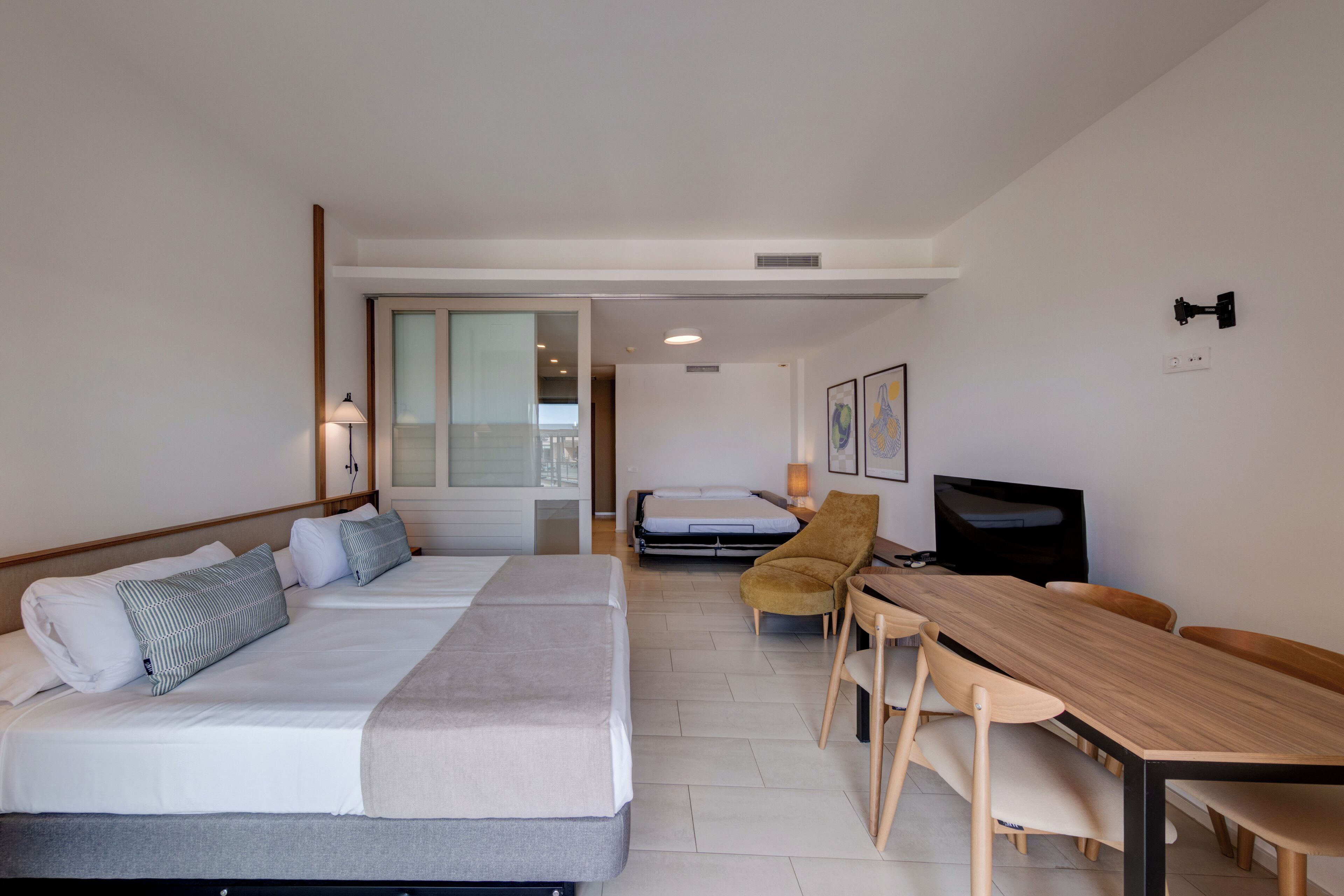Habitación de hotel con dos camas, una mesa de comedor, un televisor y una ventana.