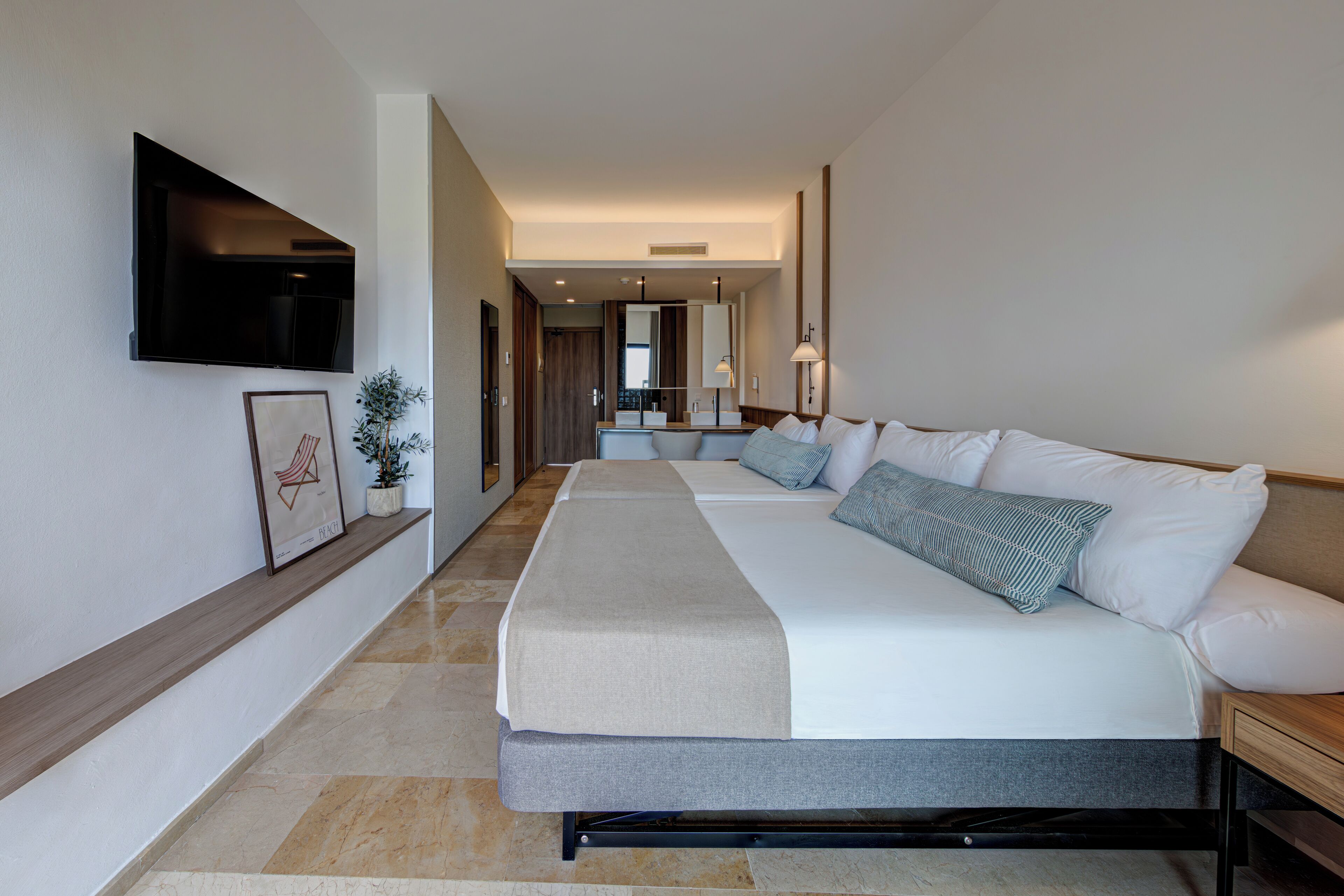 Una habitación de hotel moderna con una cama grande, un televisor montado en la pared y un pasillo que conduce a un baño.
