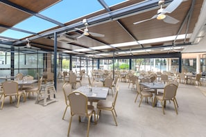 A spacious indoor dining area with multiple tables and chairs, large windows, and ceiling fans. - Ohtels Les Oliveres (El Perello)