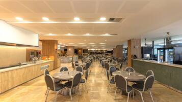 Un restaurante espacioso con varias mesas y sillas, una zona de cocina y una barra.