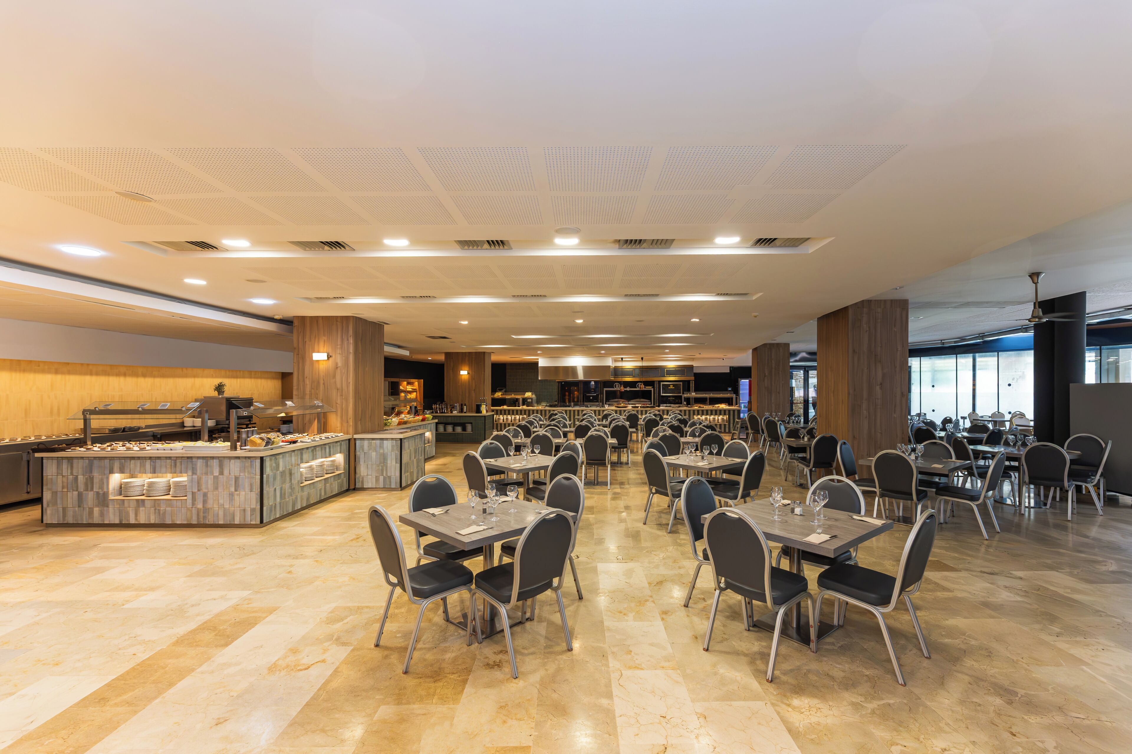 Een ruime restaurantruimte met meerdere eettafels en stoelen, een buffetgedeelte en een modern plafondontwerp.