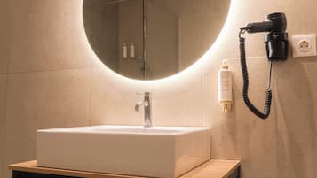 Un baño moderno con un espejo redondo grande, un lavamanos blanco y un secador de pelo montado en la pared.