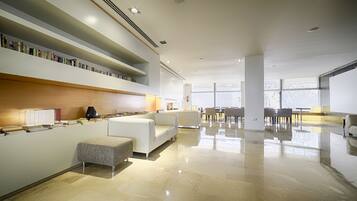 A modern, well-lit lobby with a seating area, a coffee table, and a bookshelf.