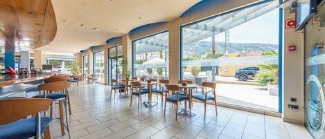 A spacious indoor area with a bar, seating, and large windows offering a view of the outside.