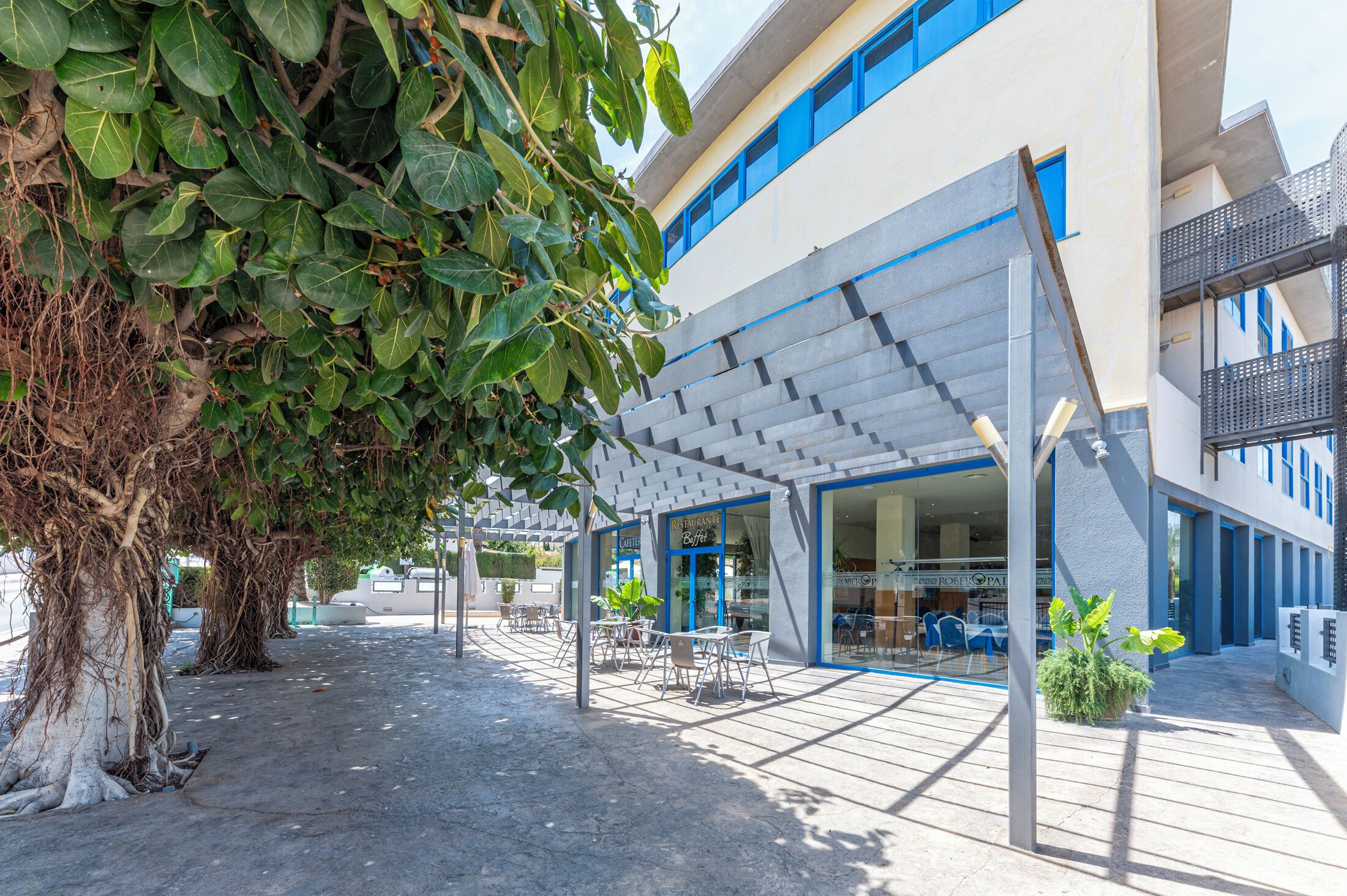 A modern building with a covered outdoor seating area, a café, and a visible entrance.