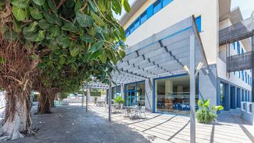 A modern building with a covered outdoor seating area, a café, and a visible entrance.