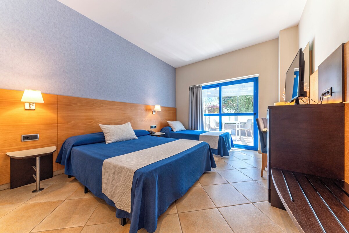 Habitación de hotel con dos camas, un escritorio, un televisor y una ventana con vistas al exterior.