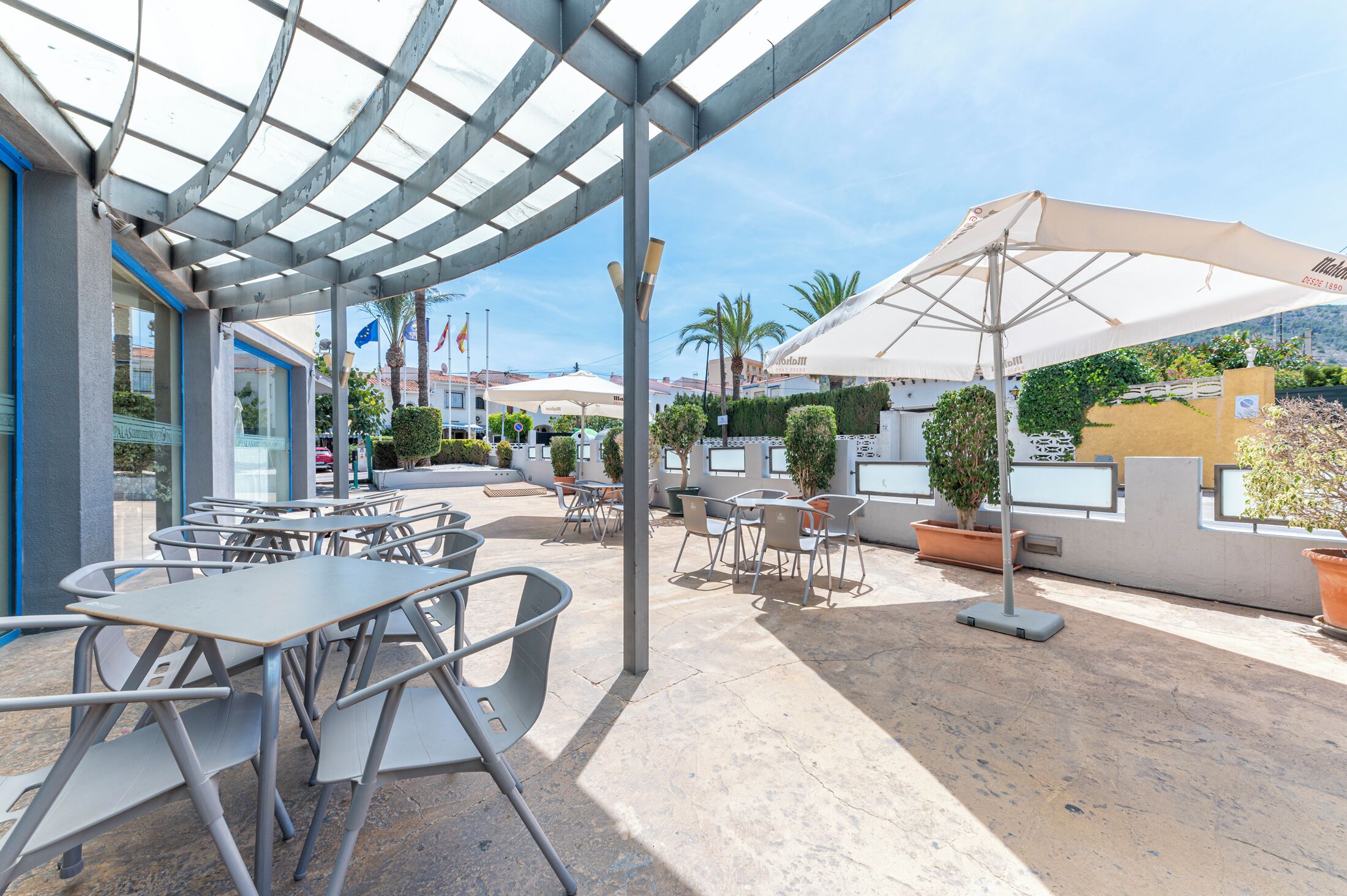An outdoor patio area with tables and chairs, umbrellas, and potted plants.