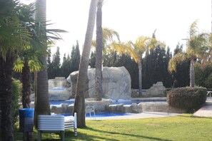 A landscaped area with palm trees, a rock formation, and a small pool. - Hotel Rober Palas (L'Alfas del Pi)