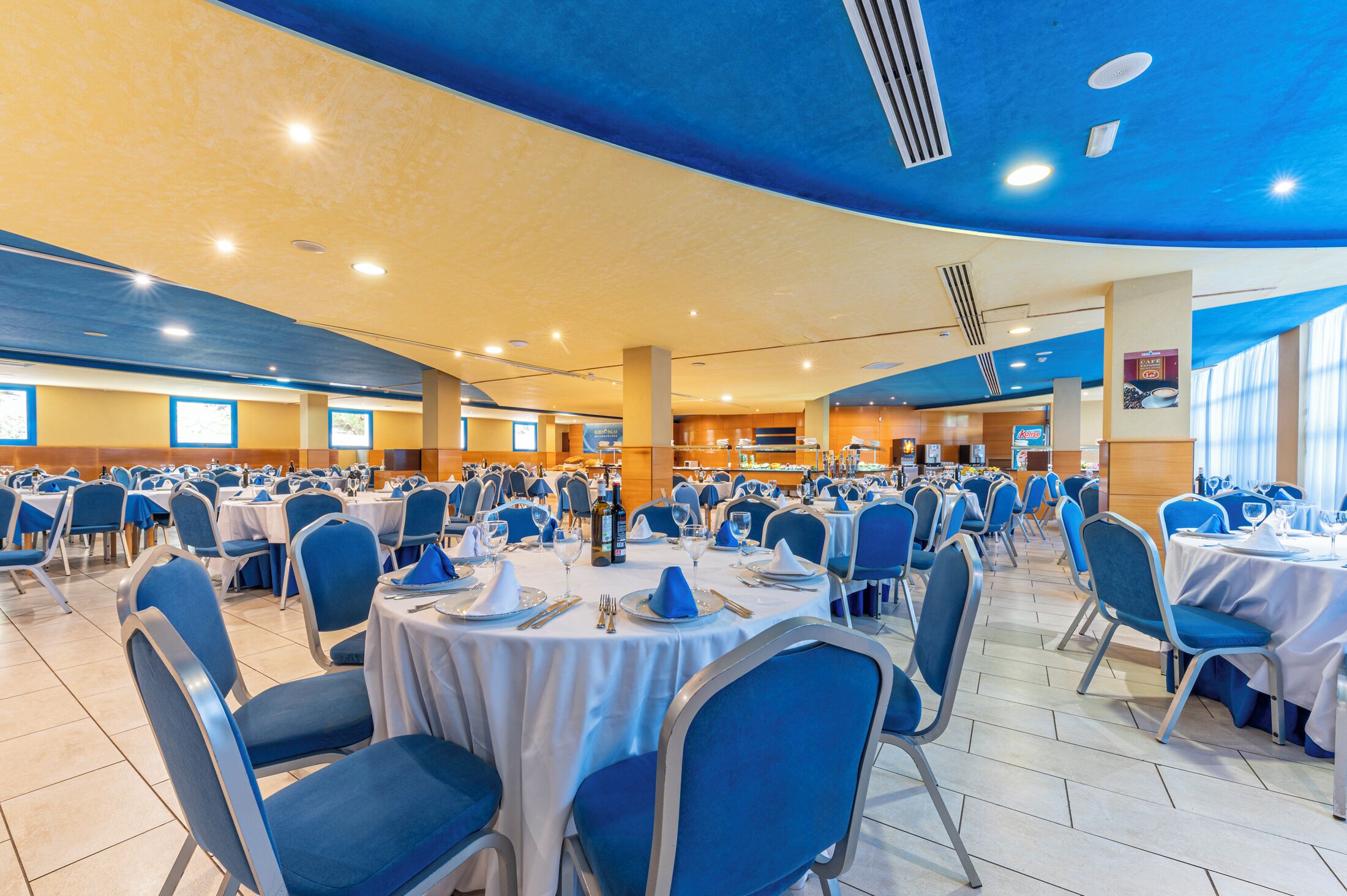 A banquet hall with round tables set for dining, blue chairs, and a ceiling with recessed lighting.