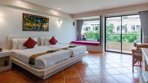 A hotel room with a large bed, a painting on the wall, and a balcony with a view of greenery. - Karon Sea Sands Resort (Karon)