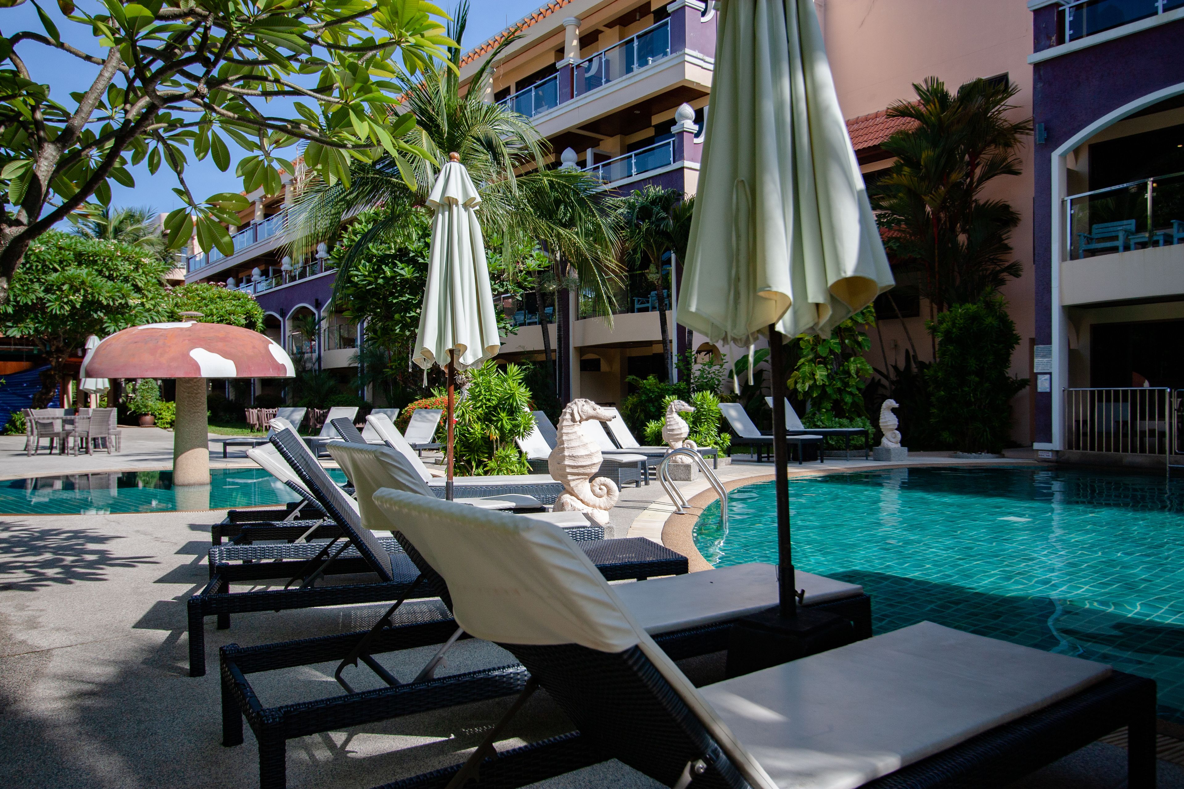 A poolside area with lounge chairs and umbrellas, a statue, and a building with balconies in the background.