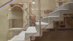Una escalera con barandilla de vidrio que conduce a una habitación con pared de azulejos y una ventana.