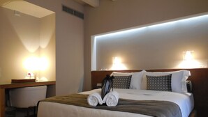 Una habitación de hotel con una cama grande, dos lámparas de noche, un cabecero de madera y un escritorio con un espejo y una lámpara.