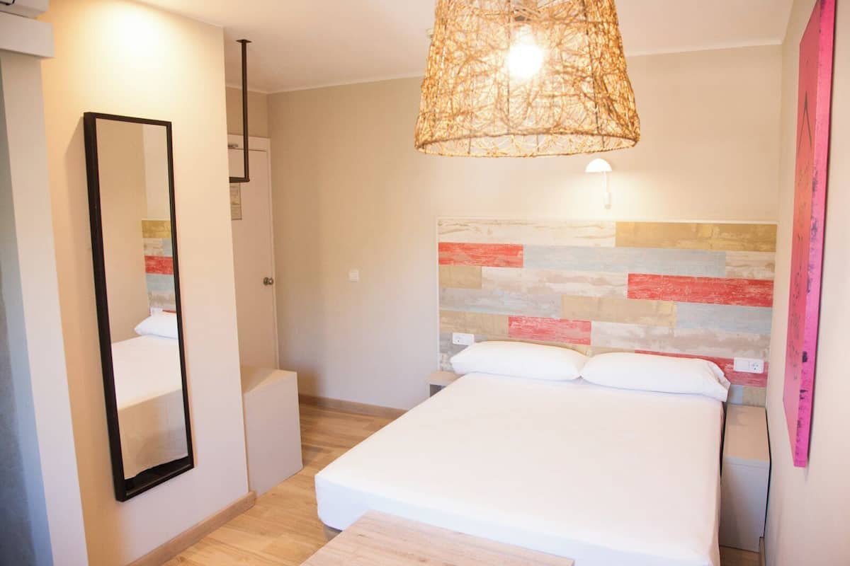 A bedroom with a bed, a mirror, a hanging light fixture, and a wall with a striped pattern.