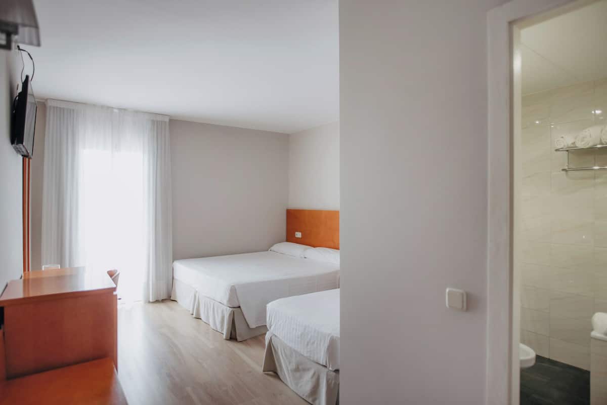 A hotel room with two beds, a desk, and a shower area.