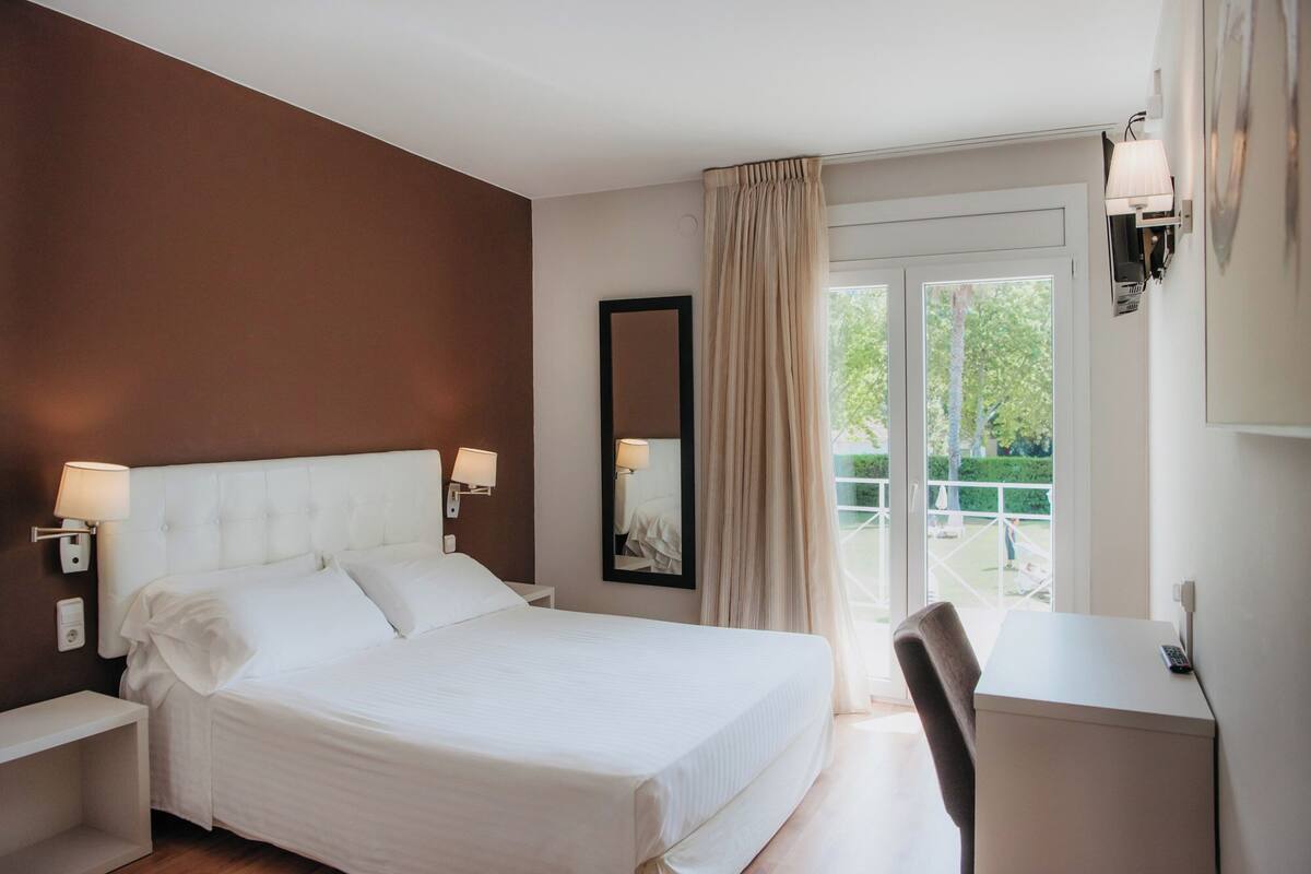 A hotel room with a bed, bedside lamps, a desk, and a view of the outdoors.